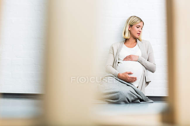 Embarazo a término joven sentada en el suelo - foto de stock