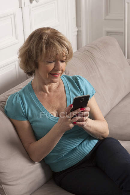 Frau benutzt Smartphone auf Sofa im Haus — Stockfoto