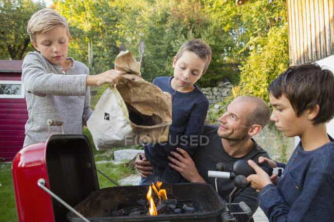 Homem adulto médio e filhos preparando churrasco no jardim — Fotografia de Stock