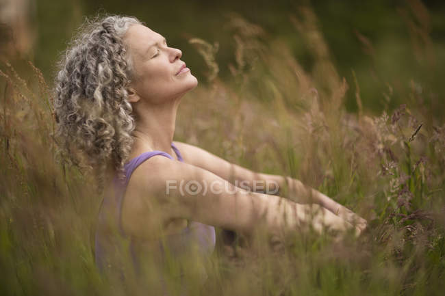 Mujer madura meditando en hierba larga - foto de stock