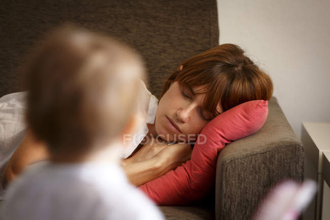 Mitte erwachsene Frau schläft auf Sofa beobachtet von Kleinkind Tochter — Stockfoto