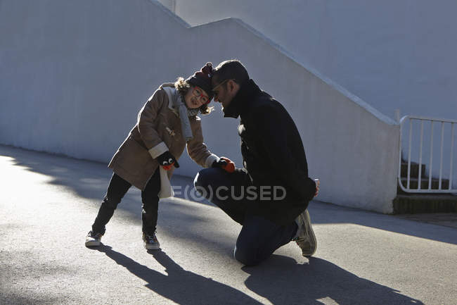 Padre e hija llevando abrigo de lona cabeza a cabeza en la calle - foto de stock