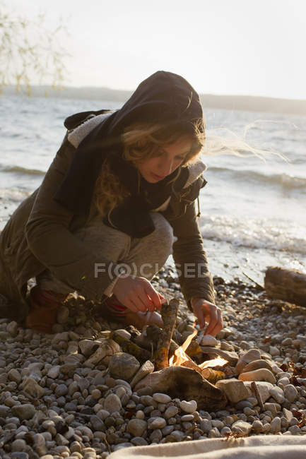 Woman making a fire by seaside — Stock Photo