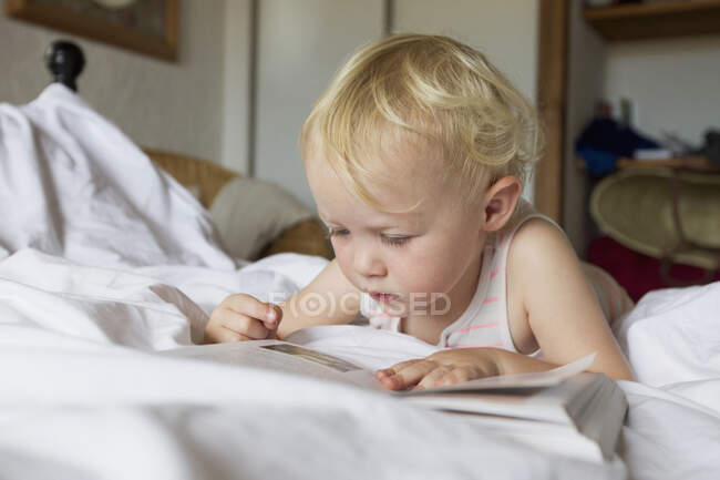 Menina deitada na cama lendo um livro — Fotografia de Stock