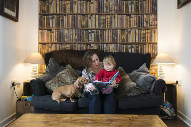 Madre leyendo libro a hijo en sofá - foto de stock