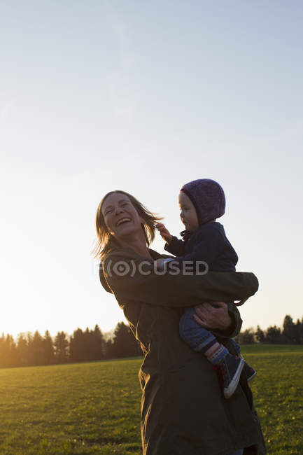 Зрелая мать и маленькая дочь смеются в поле на закате — стоковое фото