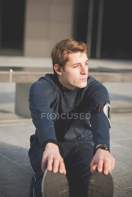 Young male doing touch toe warm ups in city square — Stock Photo