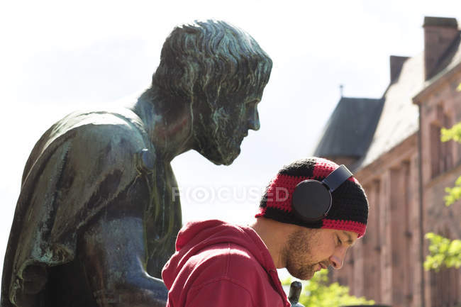 Head and shoulder portrait of mid adult man wearing headphones in front of sculpture, Freiburg, Baden, Germany — стокове фото