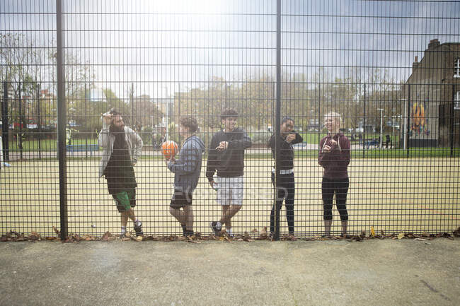 Gruppo di giovani adulti che si prendono una pausa dallo sport, appoggiati alla recinzione — Foto stock
