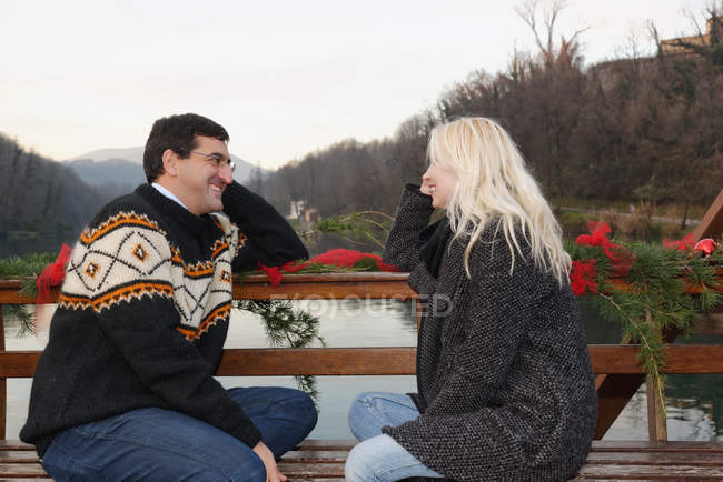 Coppia eterosessuale seduta faccia a faccia sulla panchina, accanto al lago, Lombardia, Italia — Foto stock