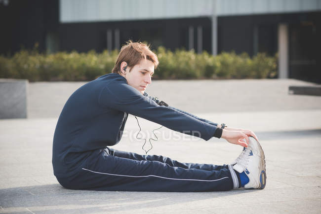 Young man touching toes in city square — Stock Photo