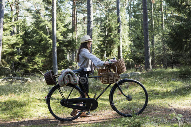 Mujer madura ciclista con cestas de forrajeo en el camino del bosque - foto de stock