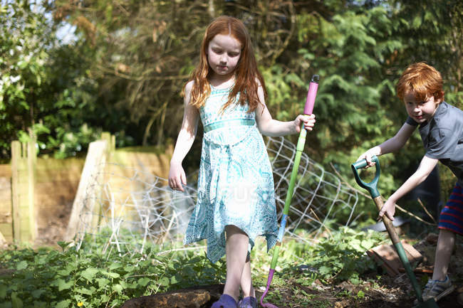 Two young children in garden, holding gardening tools — Stock Photo