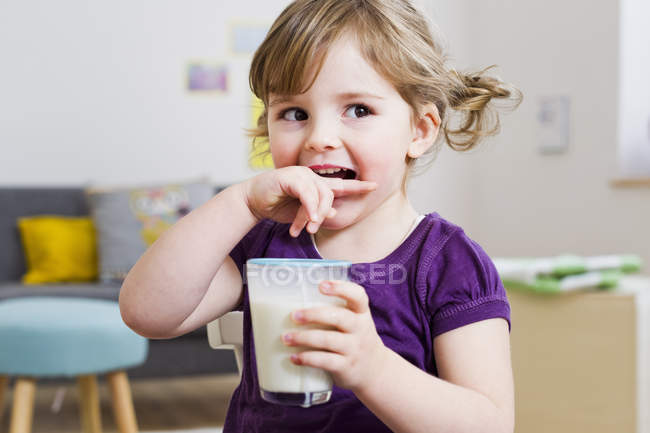 Menina segurando copo de leite em casa — Fotografia de Stock