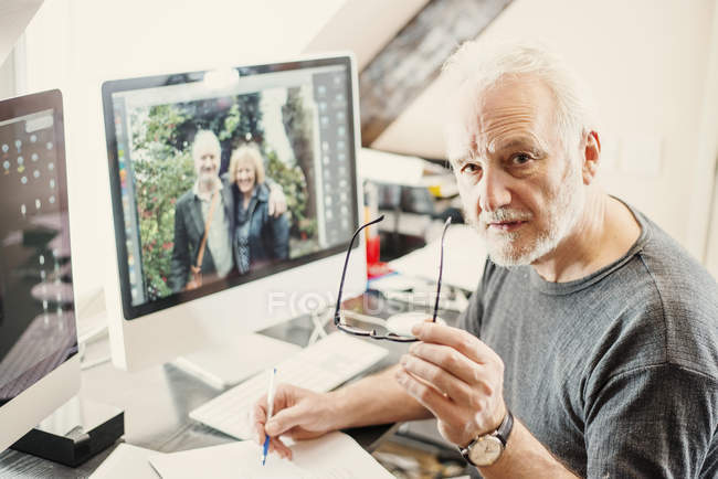 Homme âgé travaillant à la maison et regardant la caméra, vue grand angle — Photo de stock