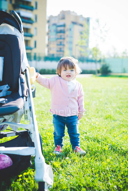 Female toddler holding onto pushchair in park — Stock Photo