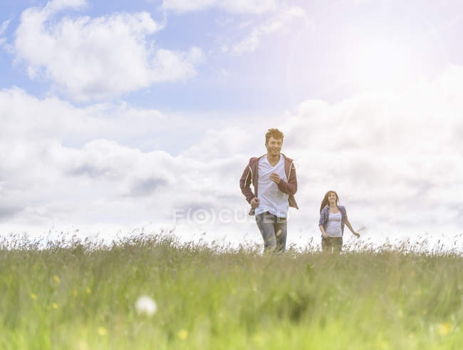 Adolescente casal correndo através do prado sob luz do sol brilhante — Fotografia de Stock