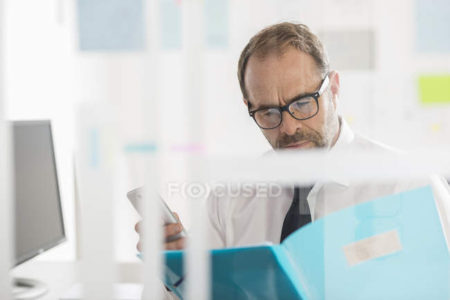 Uomo d'affari che legge documenti e utilizza smartphone — Foto stock