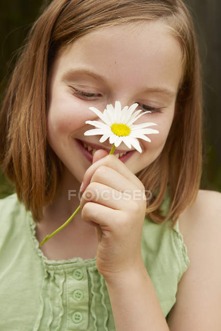Portrait of girl in garden holding up daisy — Stock Photo