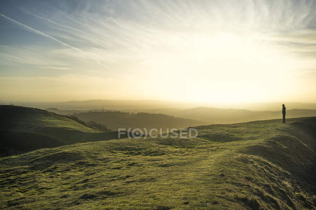 Verdes colinas onduladas con silueta de persona en la luz del atardecer - foto de stock