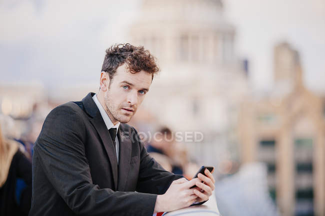 Uomo d'affari che scrive su smartphone mentre si appoggia sul Millennium Bridge, Londra, Regno Unito — Foto stock
