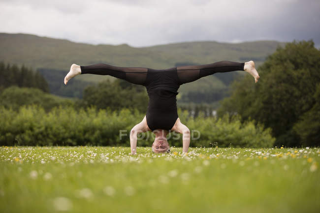 Mature woman practicing yoga standing on head with legs open in field — Stock Photo