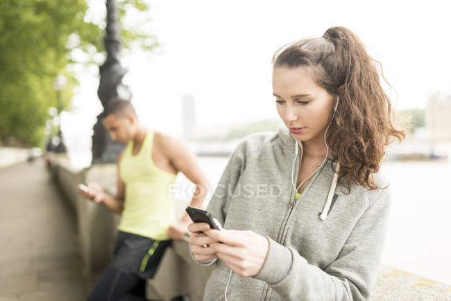 Два бігуна пишуть смартфони на березі річки. — стокове фото