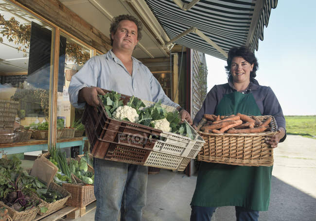 Retrato de casal de agricultura biológica com cestas de vegetais orgânicos fora da loja da fazenda — Fotografia de Stock