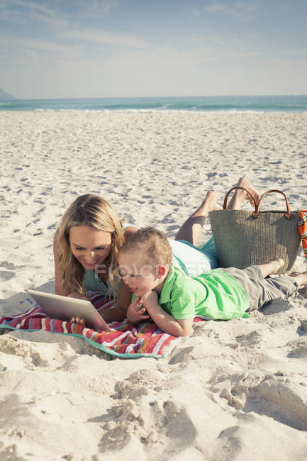 MID дорослий мати дивиться на цифровий планшет з маленьким сином на пляжі, Кейптаун, Західна Капська провінція, Південна Африка — стокове фото