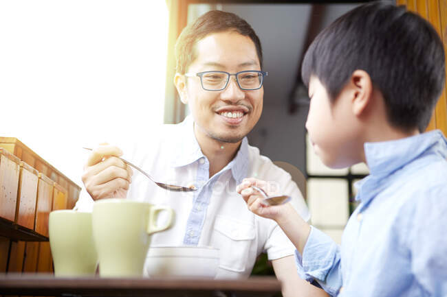 Pai chinês e filho jovem tomando café da manhã na varanda ao sol juntos — Fotografia de Stock