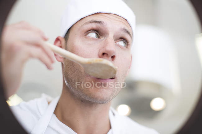 Male chef tasting food from saucepan in commercial kitchen — Stock Photo