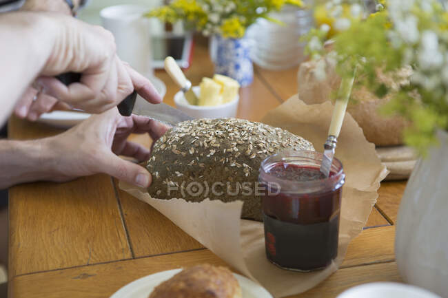 Homem cortando pão de celeiro em preparação para o café da manhã, foco em mãos — Fotografia de Stock