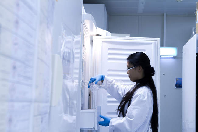 Científica seleccionando muestra refrigerada en laboratorio - foto de stock