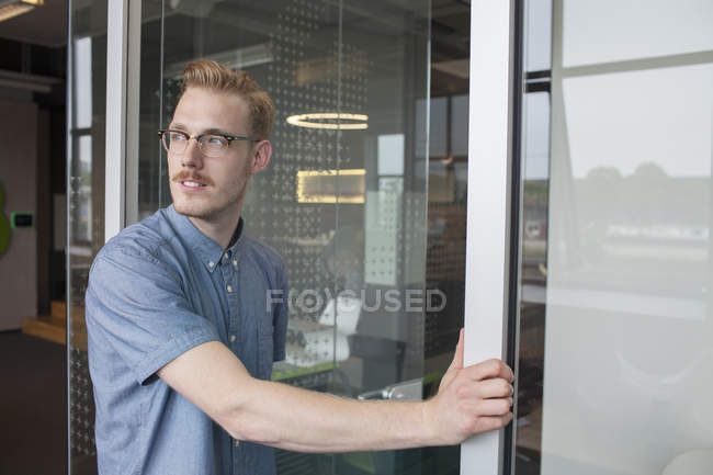 Jovem olhando ombro a ombro pela porta do escritório — Fotografia de Stock