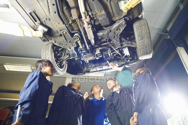 Cinco estudantes universitários olhando para cima de baixo do carro na oficina de garagem — Fotografia de Stock