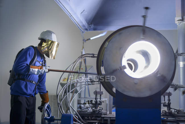 Worker forming large glass tube on lathe in glass factory — Stock Photo