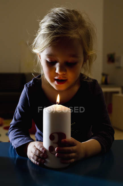 Girl holding lit candle in dark room — Stock Photo