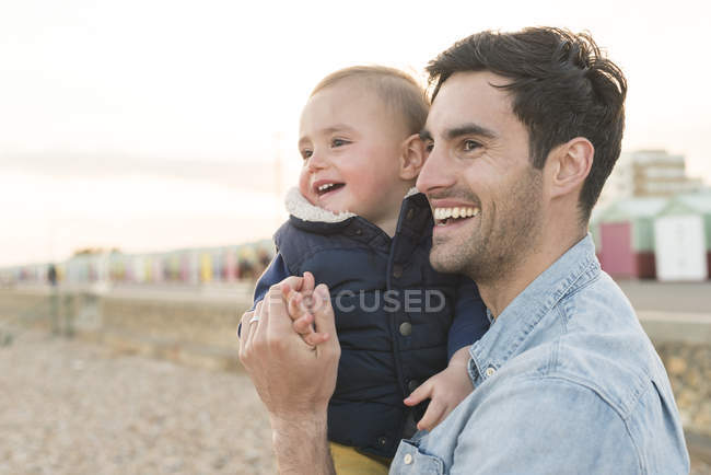 Padre sosteniendo hijo joven en la playa - foto de stock
