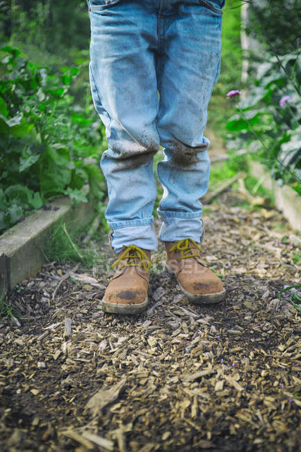 Legs of boy in dirty knee jeans on allotment — Stock Photo