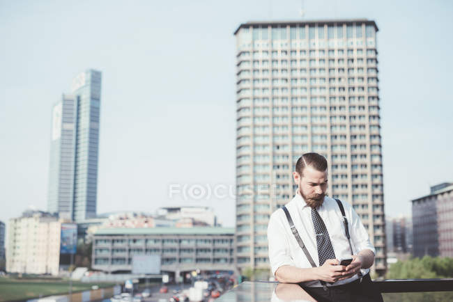 Stylish businessman reading smartphone text update on office balcony — Stock Photo