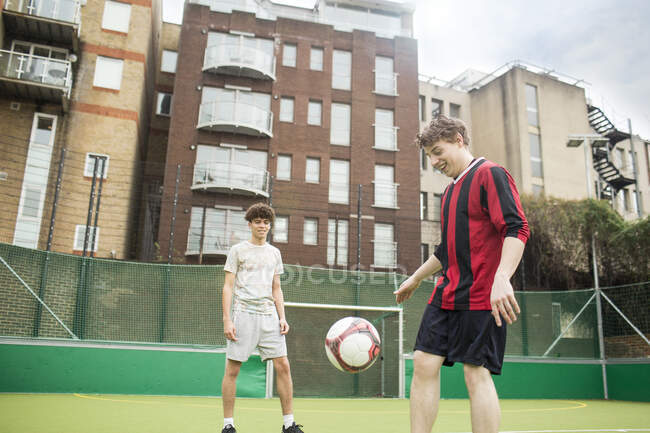 Deux jeunes hommes jouant au football sur un terrain de football urbain — Photo de stock