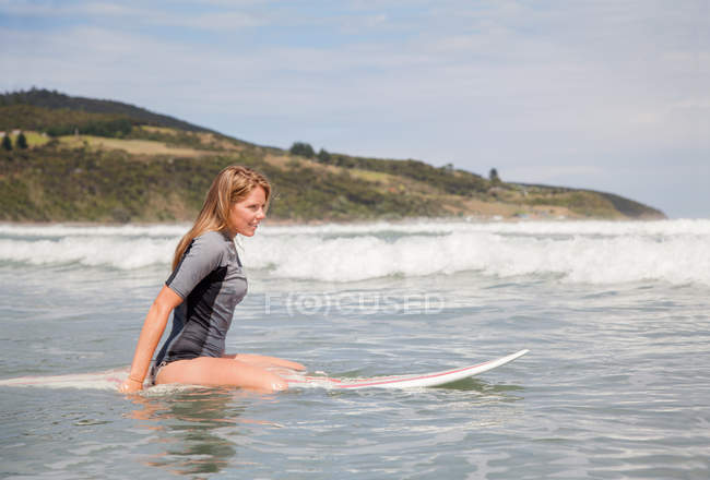 Retrato de uma jovem mulher sentada na prancha de surf no mar — Fotografia de Stock