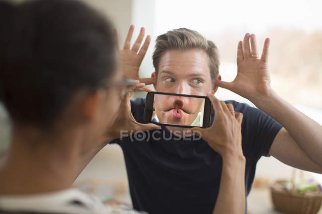 Woman holding smartphone in front of man mouth — Stock Photo