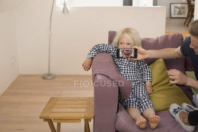 Homem segurando smartphone na frente da boca do menino — Fotografia de Stock
