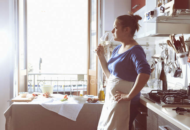 Mid adult woman taking a cooking break and drinking white wine in kitchen — Stock Photo