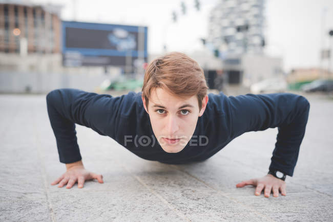 Retrato de jovem corredor do sexo masculino fazendo flexões na praça da cidade — Fotografia de Stock