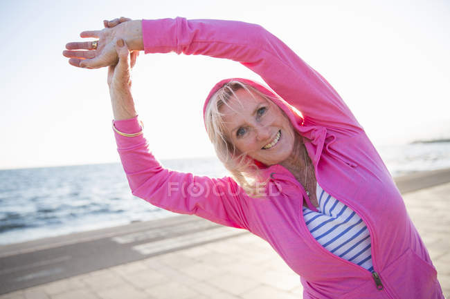Mujer mayor estirándose por la playa - foto de stock