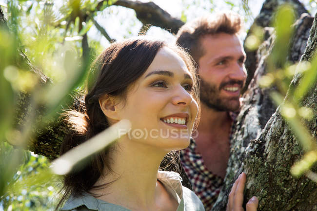 Pareja joven en el árbol mirando hacia otro lado sonriendo - foto de stock