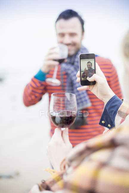 Couple drinking wine, woman taking photo of man outdoors — Stock Photo