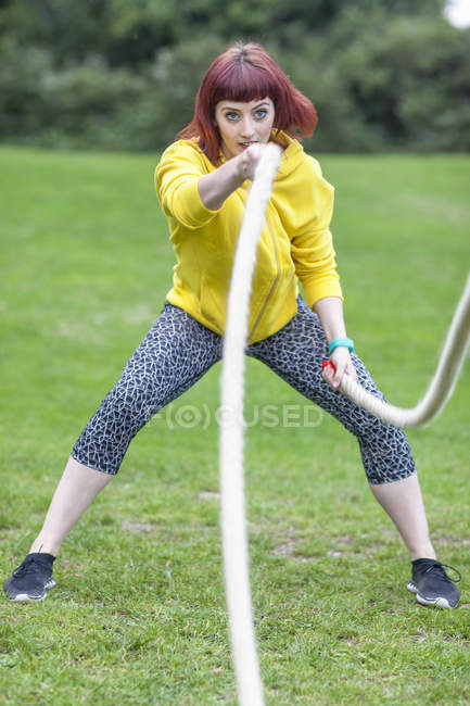 Junge Frau zieht Seil auf Feld — Stockfoto